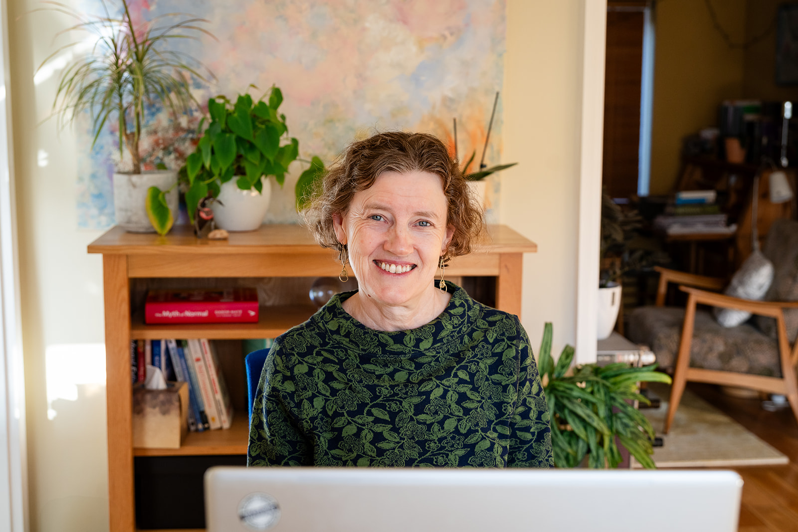 Sorrel Pindar wearing a green top, sitting in front of her laptop and looking up at you