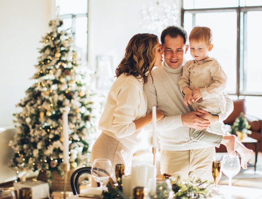 Couple with baby at a table laid for Christmas with a Christmas tree behind them